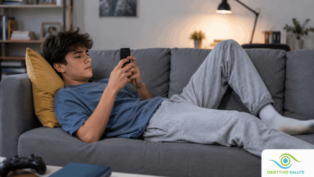 Un giovane ragazzo, sdraiato con una postura scorretta sul divano, mentre gioca allo smartphone